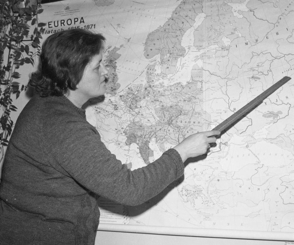 Nauczycielka wskazuje linijką miejsce na dużej mapie Europy. O szkole w czasach PRL-u przeczytasz w serwisie Eska.
