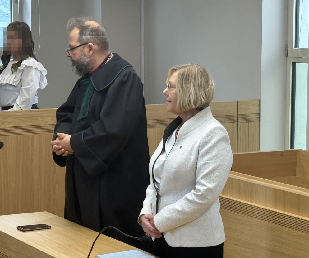 Barbara Nowak w białym żakiecie stoi obok adwokata w sali sądowej. O wyroku skazującym kurator przeczytasz na SE.