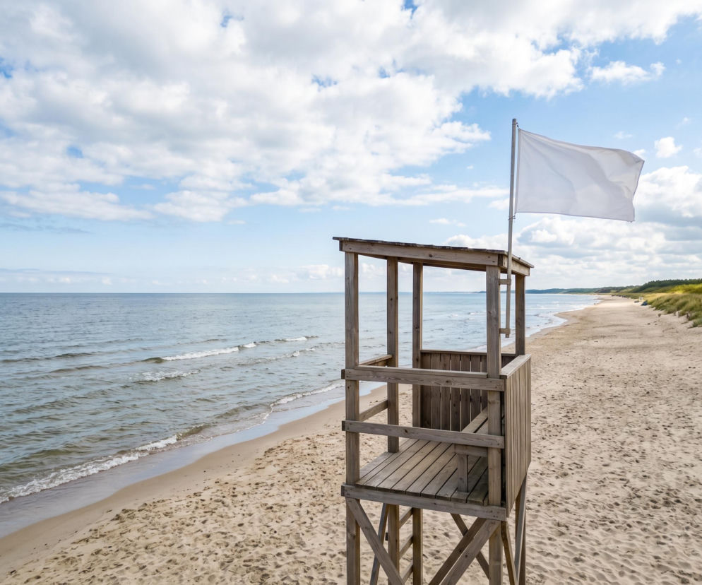 Drewniana wieża ratownicza z białą flagą na pustej plaży w Rewalu. O warunkach nad wodą przeczytasz na SE Szczecin.