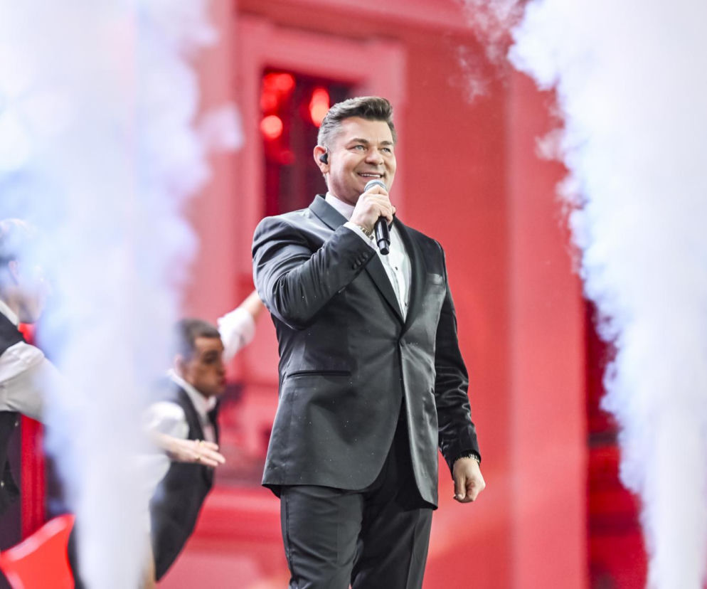Uśmiechnięty Zenon Martyniuk śpiewa do mikrofonu na scenie wśród dymu. O sporze z Jackiem Kawalcem przeczytasz na SE.