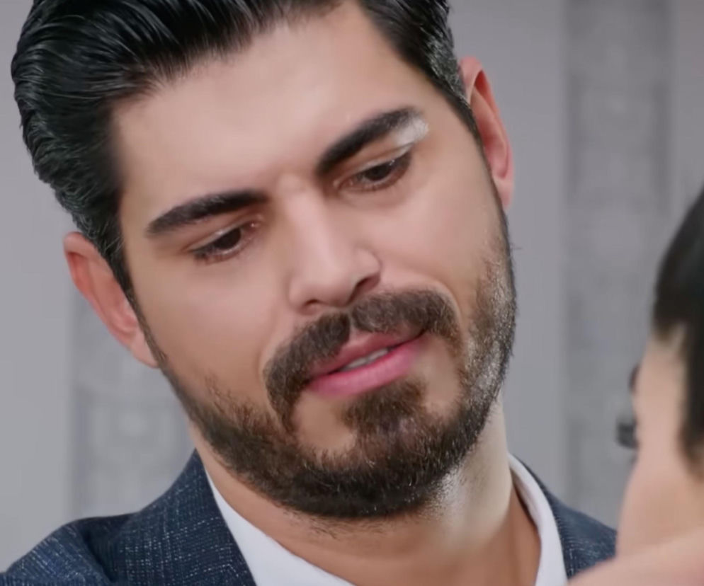 Turecki aktor Türkseve jako Cihan w serialu „Panna młoda”, ubrany w granatową marynarkę i białą koszulę, spogląda z uśmiechem w dół. Ta scena z 73. odcinka, gdzie Cihan obdarowuje Hancer, jest opisana szczegółowo na portalu Super Seriale.