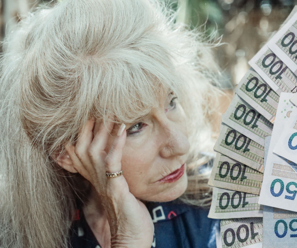 Zamyślona seniorka trzyma rękę przy twarzy. Obok wachlarz banknotów. O walce o emerytury przeczytasz na Eska.