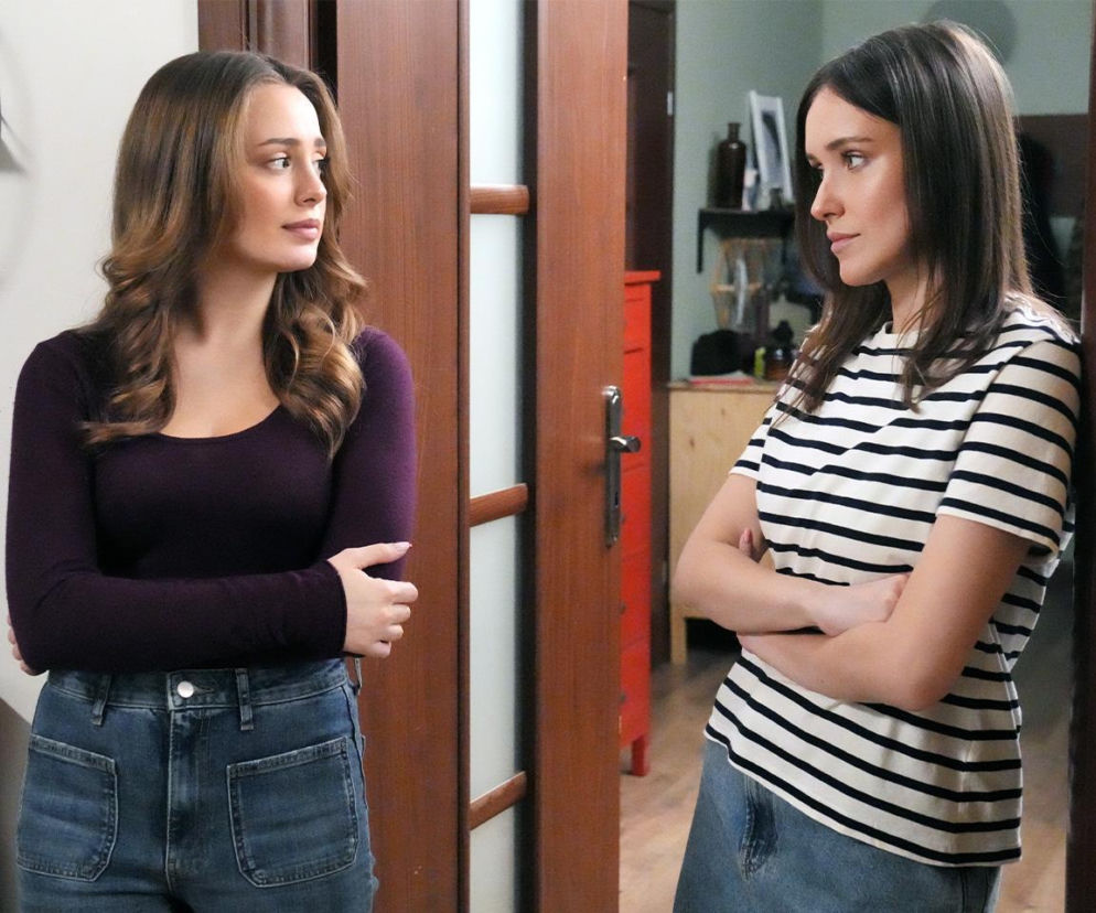 Aktorki Wiktoria Gąsiewska jako Oliwka (w purpurowej bluzce) i Natalia Sierzputowska jako Madzia (w bluzce w paski) w scenie z serialu Barwy szczęścia, stoją do siebie bokiem w pomieszczeniu z drewnianymi drzwiami. Oliwka i Madzia są skonfliktowane w odcinku 3354. Więcej na Super Seriale.