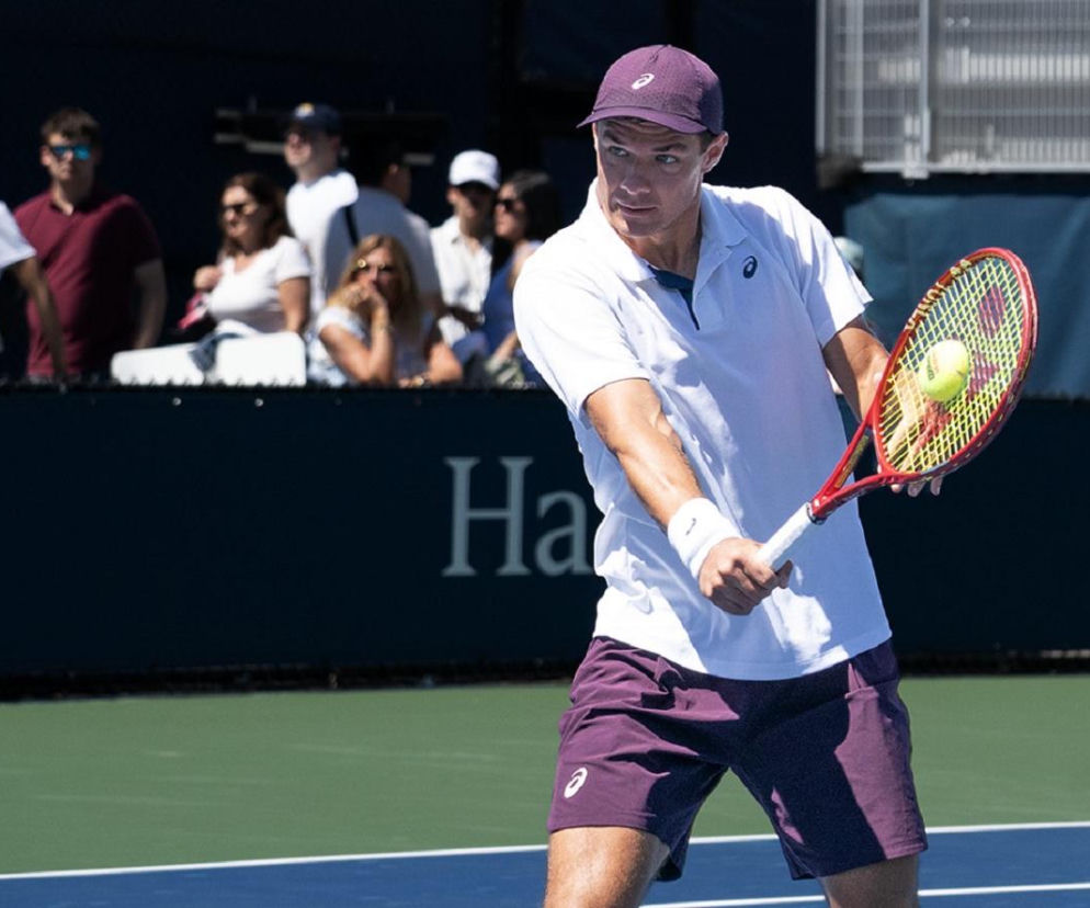 Kamil Majchrzak w białej koszulce odbija piłkę rakietą podczas US Open. O jego zwycięstwie przeczytasz na SE Supersport.