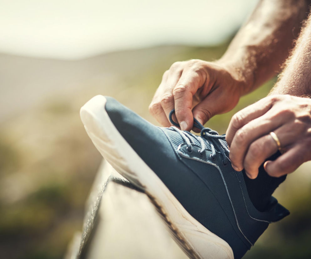 Mężczyzna w sportowych butach zawiązuje sznurówki, przygotowując się do aktywności fizycznej na świeżym powietrzu. Regularny ruch to klucz do niższego ryzyka cukrzycy typu 2, o czym przeczytasz na Poradnik Zdrowie.