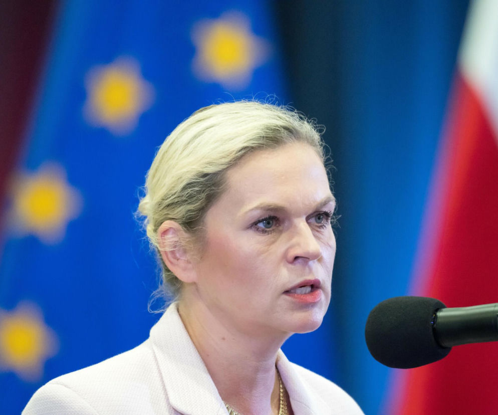 Minister edukacji Barbara Nowacka przemawia do mikrofonu na tle flagi Unii Europejskiej. O sporze z Kościołem przeczytasz w Eska.