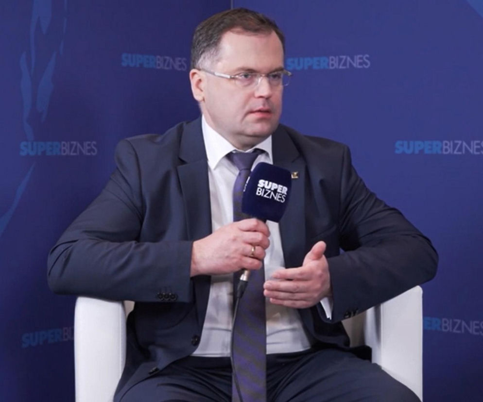 Tadeusz Białek, prezes Związku Banków Polskich, podczas wywiadu. Mężczyzna siedzi na białym fotelu, ubrany w ciemny garnitur i krawat, trzyma mikrofon z logo Super Biznes. W tle ściana z wielokrotnie powtórzonym napisem Super Biznes.