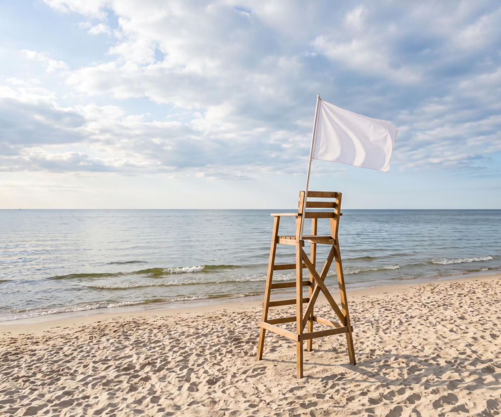 Biała flaga na wieży ratowniczej na pustej plaży w Dąbkach. O bezpieczeństwie kąpieli przeczytasz na SE Szczecin.