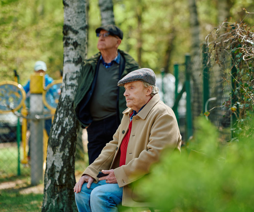 Aktor Mieczysław Hryniewicz jako Włodek Zięba siedzi na ławce w parku. O serialu Na Wspólnej przeczytasz na VOX FM.