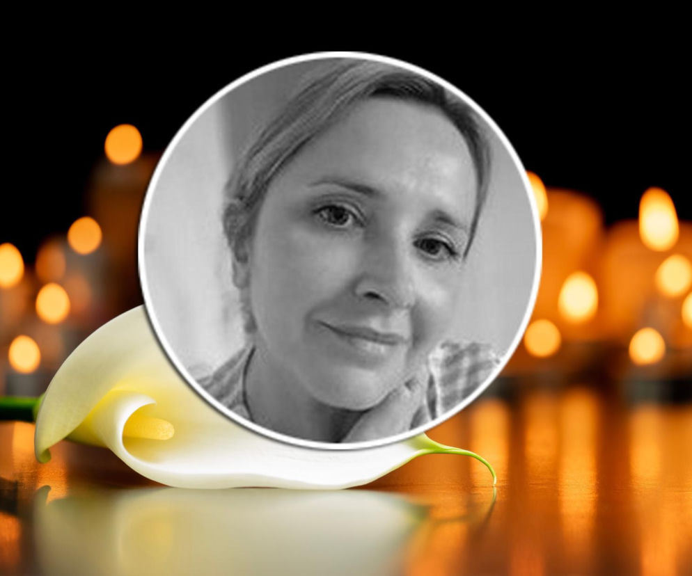 Biała kalia leżąca na stole w otoczeniu rozmytych świateł świec, symbolizująca pamięć. Na pierwszym planie, w okrągłej ramce, czarno-białe zdjęcie Katarzyny Gospodarek. Więcej o jej życiu przeczytasz na Super Biznes.