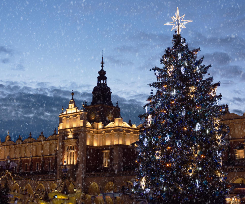 Krakowski Rynek Główny zimą, na którym stoi ozdobiona choinka z gwiazdą na szczycie. W tle oświetlone Sukiennice. Scena przedstawia malownicze miasto Kraków w kontekście powrotu groźnej choroby. Czytaj o tym, co dzieje się w Krakowie na Poradnik Zdrowie.