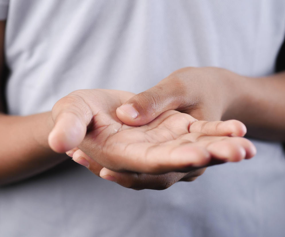 Zbliżenie na dłonie osoby z jasnym odcieniem skóry, która jedną ręką masuje drugą, sygnalizując ból lub dyskomfort związany z drętwieniem kończyn. Dowiedz się więcej o przyczynach drętwienia rąk i nóg na portalu Poradnik Zdrowie.