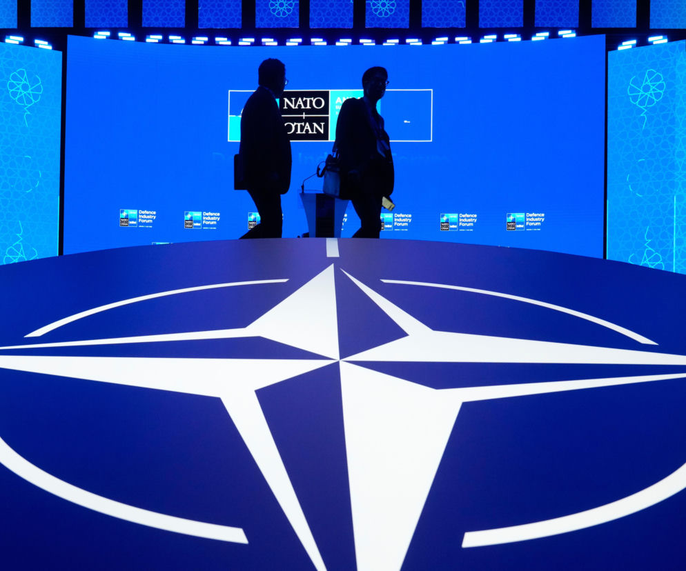 Logo NATO na podłodze forum obronnego. W tle sylwetki osób na tle ekranów. O szczycie w Ankarze na SE Portal Obronny.