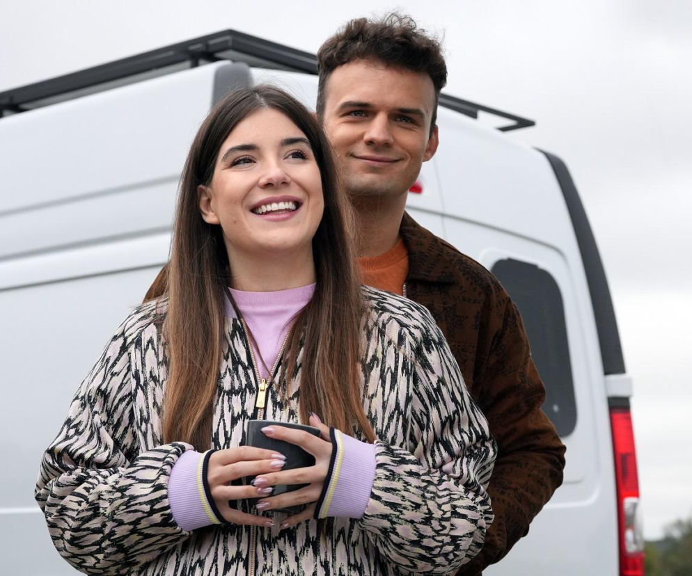 Agata Pyrka (Natalia Zambrzycka) uśmiecha się radośnie, trzymając kubek w dłoniach, a Ignacy Kieliszewski (Olaf Staszkiewicz) obejmuje ją od tyłu, oboje na tle białego vana. Para z serialu Barwy szczęścia planuje wspólne życie i powiększenie rodziny. Więcej na ten temat na Super Seriale.