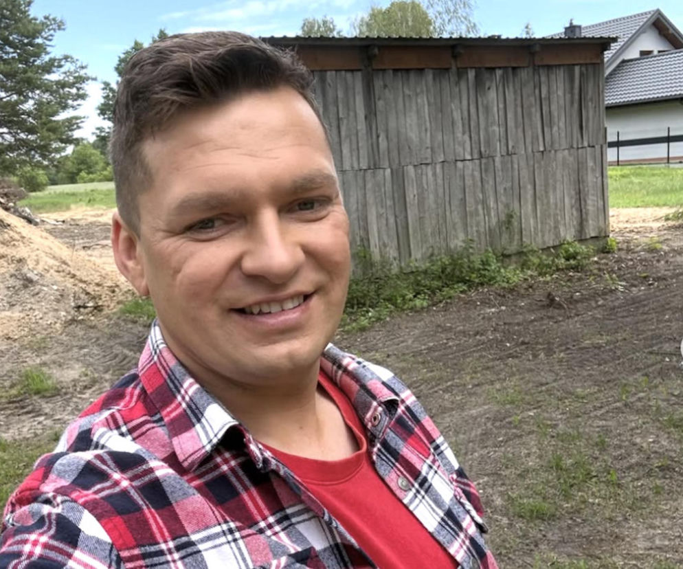 Uśmiechnięty Szymon Karaś w kraciastej koszuli na planie Farmy. O kulisach 6. sezonu przeczytasz na SE Superseriale.