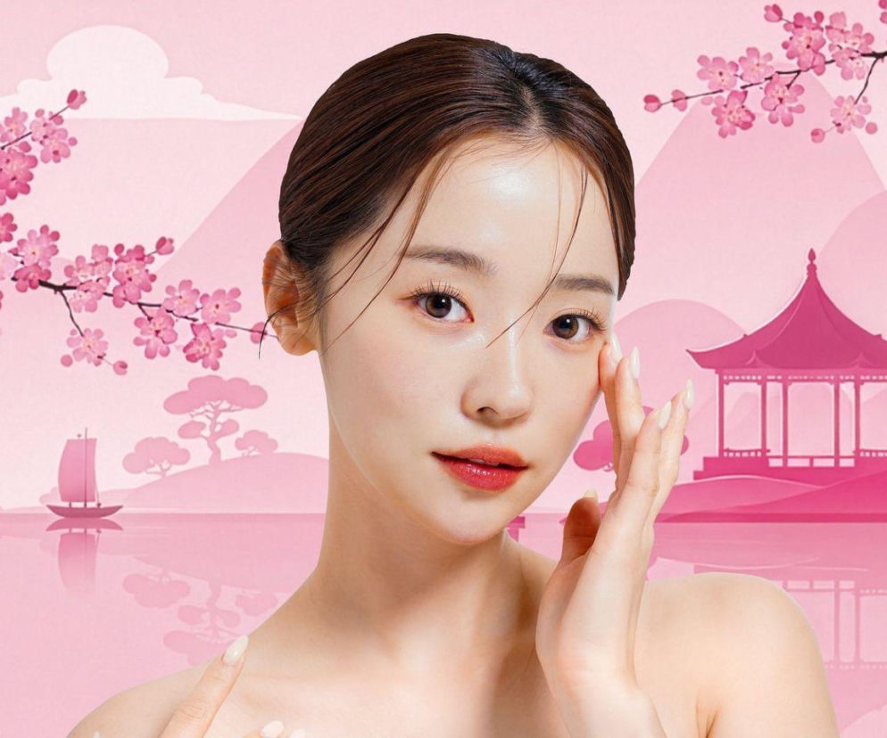 Młoda kobieta o gładkiej cerze na tle różowego koreańskiego krajobrazu. O trendach K-beauty przeczytasz na Eska.