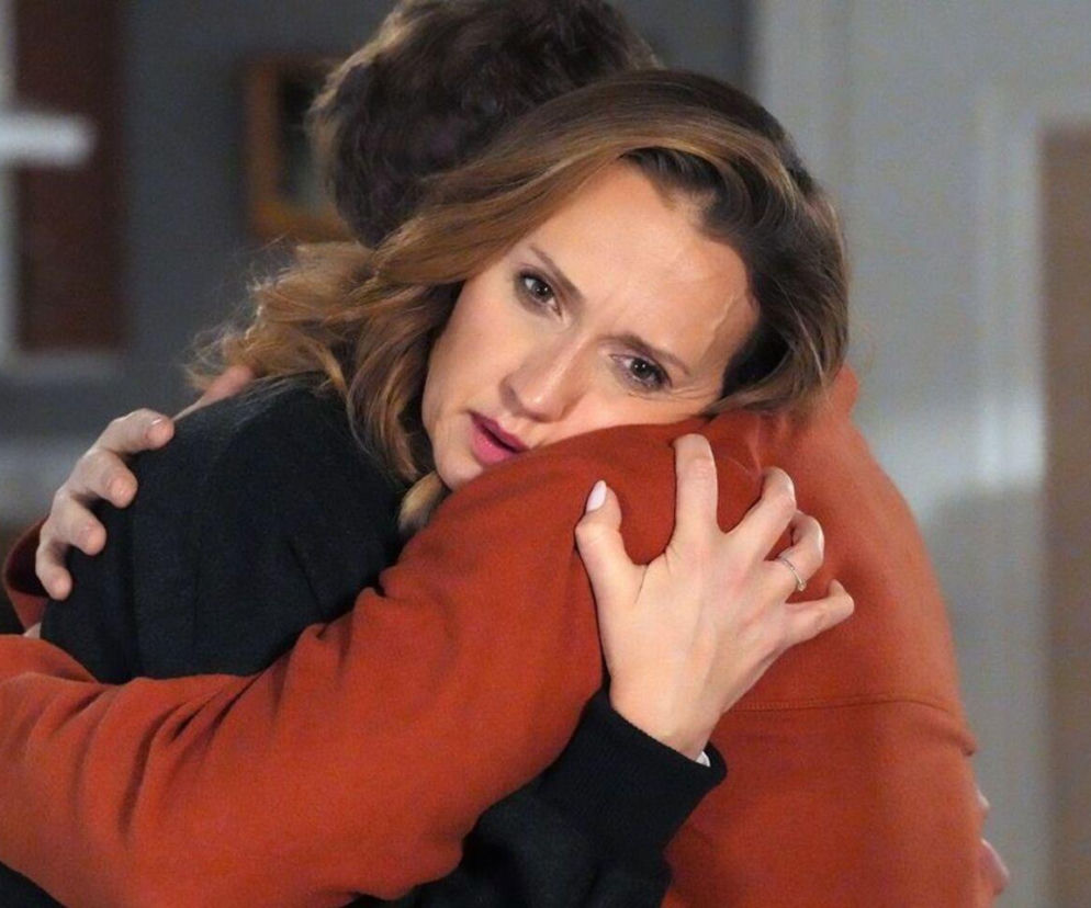 Asia (Anna Gzyra-Augustynowicz) w czarnej bluzce przytula Huberta (Marek Molak) w pomarańczowej bluzie, z zaniepokojeniem patrząc w obiektyw. Jej dłoń z pierścionkiem leży na ramieniu mężczyzny. Zdjęcie ilustruje problemy bohaterów Barw szczęścia przed wylotem do USA. Więcej na Super Seriale.