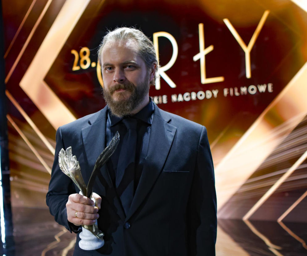 Aktor Tomasz Schuchardt z brodą trzyma statuetkę Orła na gali. O sukcesach artysty przeczytasz na SE.