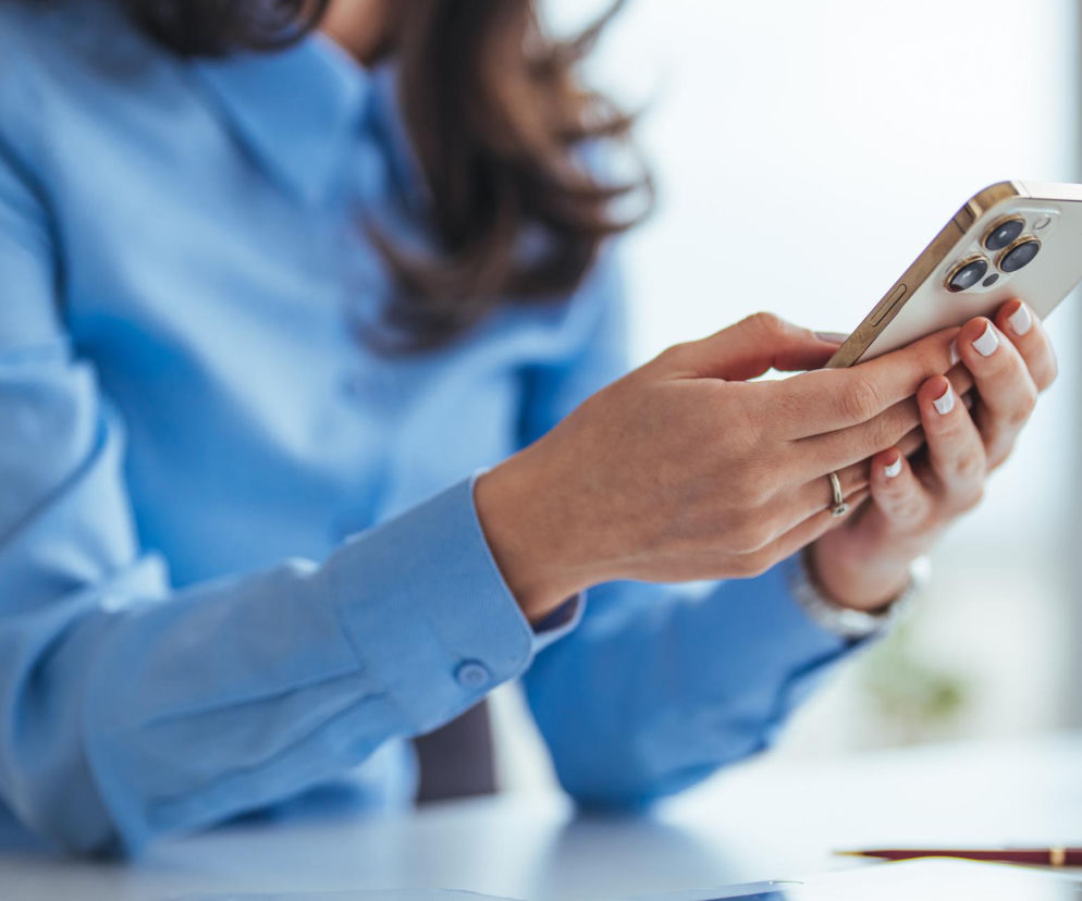 Kobieta w błękitnej koszuli trzyma smartfon z trzema obiektywami aparatu, symbolizujący proste kroki w planowaniu wizyty u lekarza. Ta metoda małych kroków pomaga przełamać prokrastynację zdrowotną i odzyskać kontrolę nad zdrowiem, o czym więcej przeczytasz na Poradniku Zdrowie.