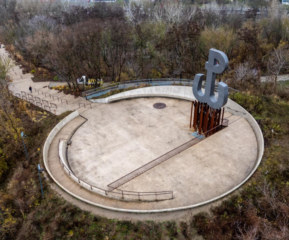 Widok z góry na Kopiec Powstania Warszawskiego w jesiennej odsłonie, z dominującym pomnikiem Polski Walczącej na okrągłej platformie. Otacza go bujna, lecz już pozbawiona liści roślinność, a ścieżki i schody prowadzą w dół. O tej wyjątkowej realizacji przeczytasz na Architektura Murator Plus.