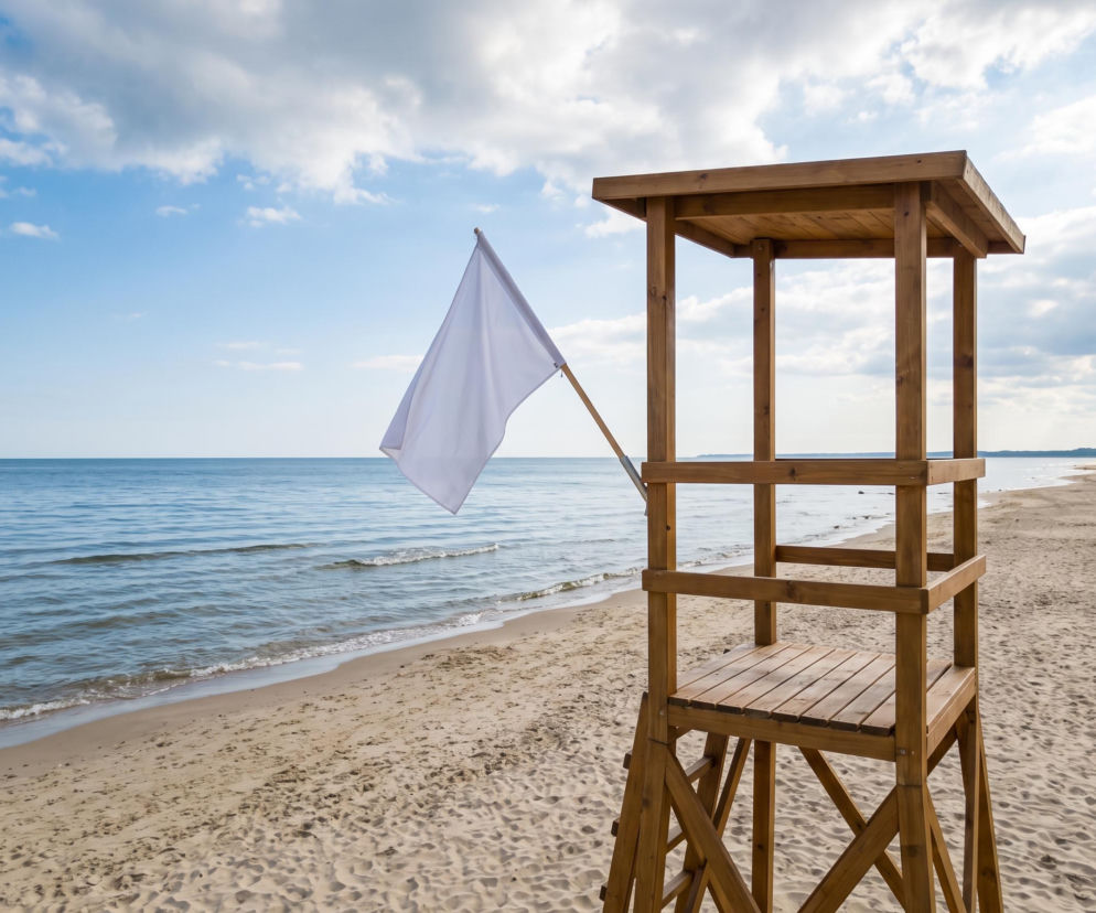 Drewniana wieża ratownicza z białą flagą na plaży w Świnoujściu. O bezpiecznej kąpieli przeczytasz na SE Szczecin.