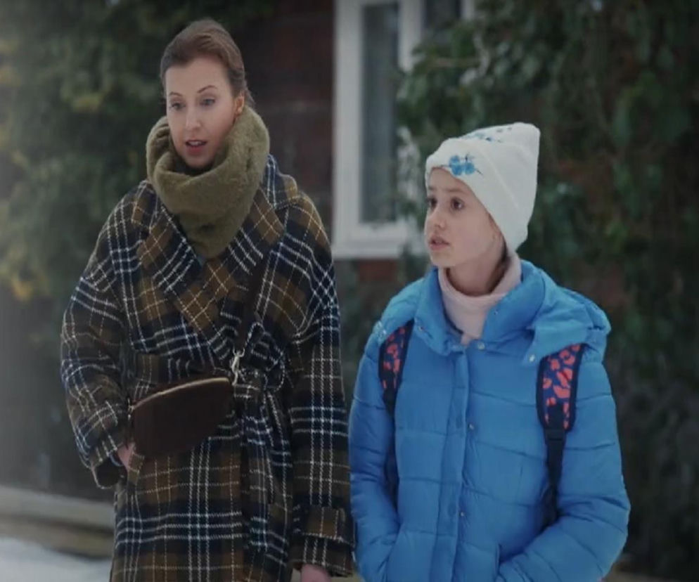Natalka (Dominika Suchecka) i Hania (Wiktoria Basik) na tle zaśnieżonego ogrodu, idące razem. Hania ma na sobie niebieską kurtkę i białą czapkę, a Natalka płaszcz w kratę. Więcej o ich losach w M jak miłość przeczytasz na portalu Super Seriale.