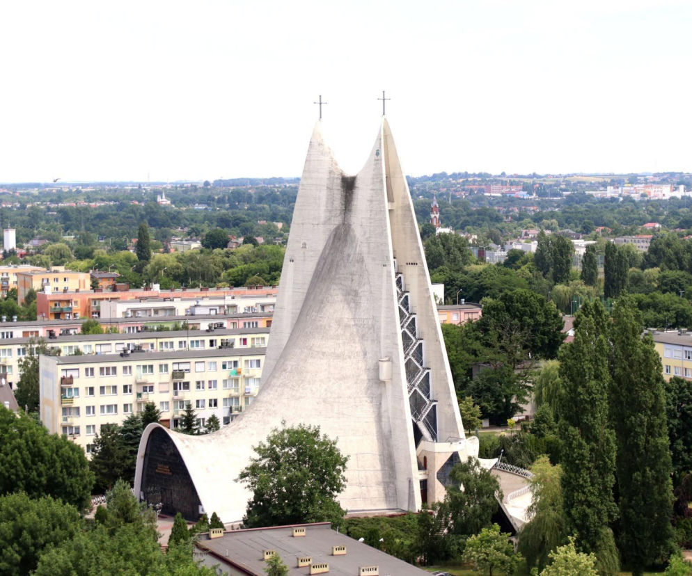 Betonowy kościół w Kaliszu o kształcie hiperboloidy na tle osiedla. O jego architekturze przeczytasz w serwisie Architektura.