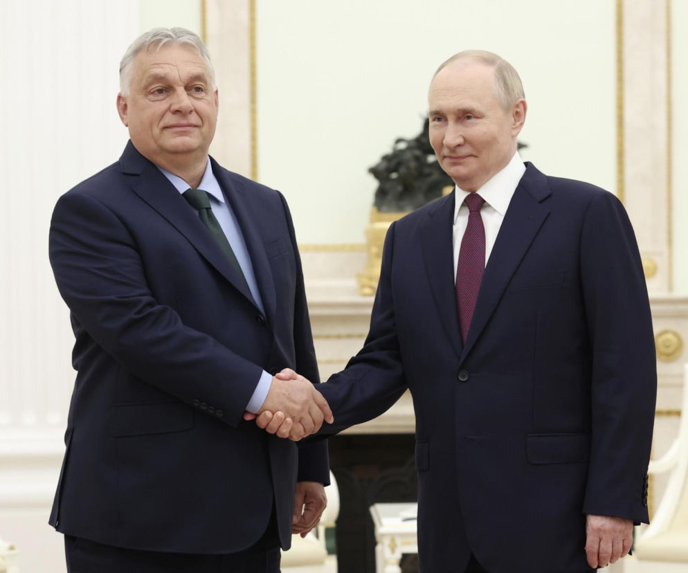 Premier Węgier Viktor Orbán i prezydent Rosji Władimir Putin uścisnęli dłonie, stojąc w eleganckim, jasnym wnętrzu. Obaj mężczyźni ubrani są w ciemne garnitury, a ich spotkanie budzi kontrowersje, o których przeczytasz na Super Biznes.