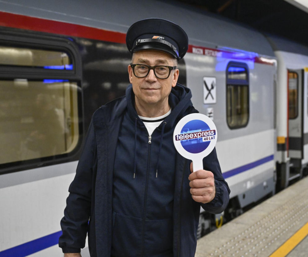 Maciej Orłoś w czapce konduktorskiej trzyma tabliczkę z logo Teleexpressu na tle pociągu. O apelu dziennikarza czytaj w SE.
