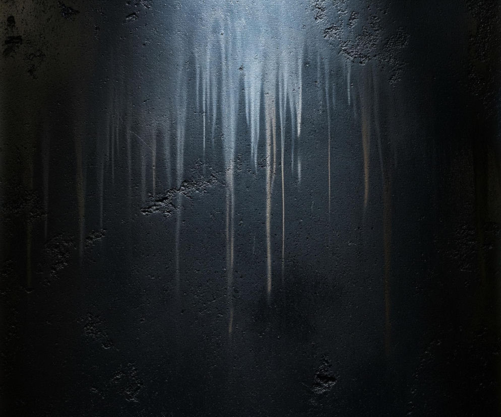 Ciemna, ziarnista, pionowa powierzchnia zajmuje centralną część obrazu. Na górze tej powierzchni widać jasne, biało-niebieskie światło, które rozciąga się w dół w postaci wielu pionowych, jasnych smug o różnej długości i grubości. Smugi są najjaśniejsze w górnej części, stają się bledsze i mniej wyraźne w miarę schodzenia w dół, a niektóre z nich mają delikatny, ciepły odcień. Krawędzie obrazu po lewej i prawej stronie są rozmyte i jaśniejsze, tworząc efekt tła, z ciemnymi, niewyraźnymi formami.