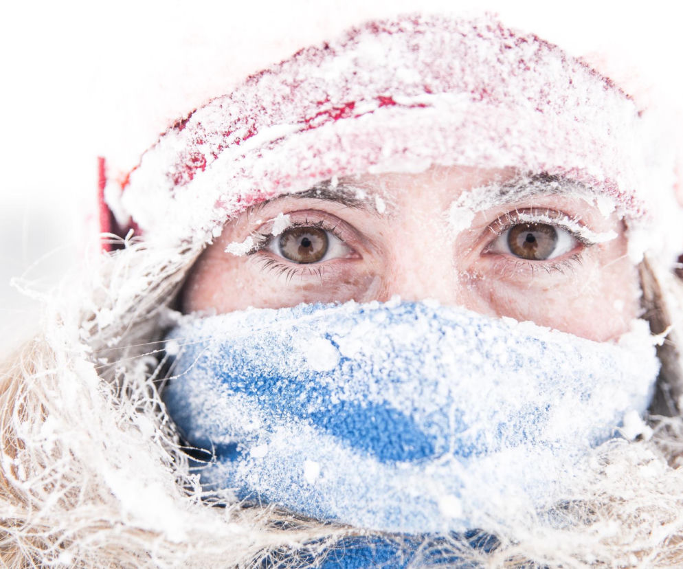 Zimno, wyziębiona kobieta w czapce i szaliku z zamarzniętymi brwiami, rzęsami i włosami, symbolizująca ekstremalne mrozy i zimę stulecia. Na portalu Poradnik Zdrowie znajdziesz informacje o wpływie niskich temperatur na zdrowie i jak się chronić.