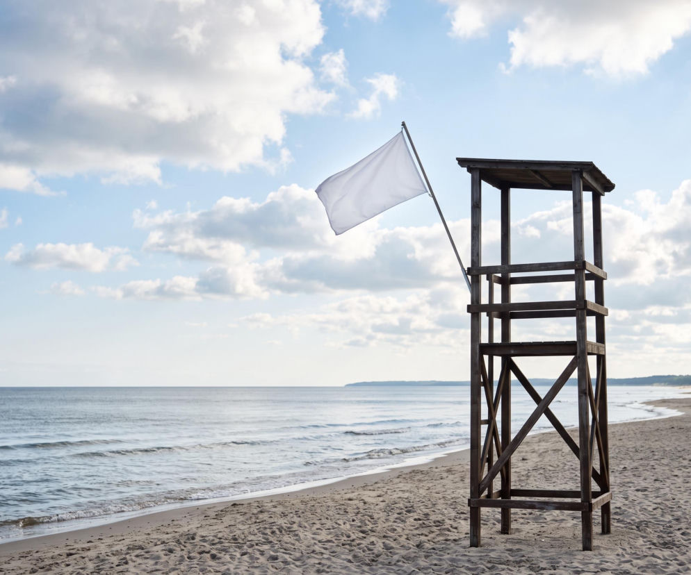 Biała flaga na wieży ratowniczej przy pustej plaży. O bezpiecznej kąpieli w Dźwirzynie przeczytasz na SE Szczecin.
