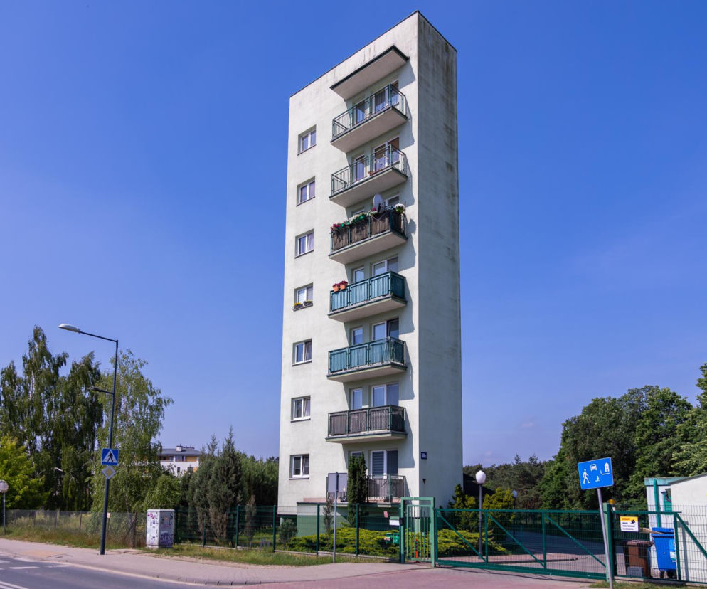 Wysoki, wąski blok mieszkalny w Warszawie, widziany pod kątem, stwarza iluzję niezwykłej smukłości. Jasnozielona elewacja i ciemne balustrady balkonów wyróżniają budynek przy ulicy Odkrytej 55C. Artykuł na Architektura Murator Plus wyjaśnia tę architektoniczną perspektywę.