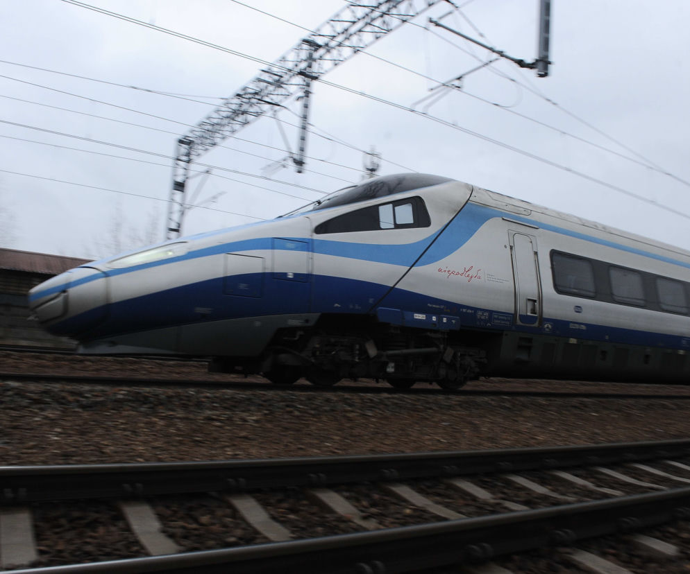 Pędzący pociąg Pendolino w barwach PKP Intercity, z napisem Niepodległa na burcie, przemieszcza się po torach kolejowych, a w tle widać sieć trakcyjną. Więcej o rozkładzie jazdy PKP Intercity przeczytasz na Super Biznes.