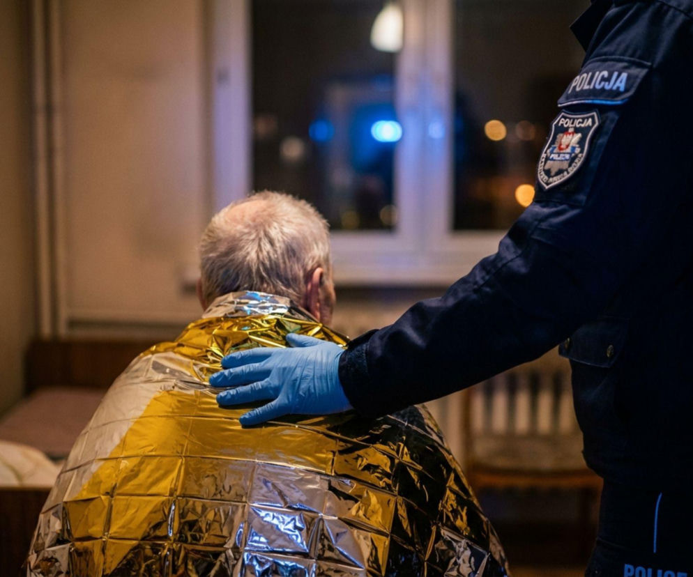 Policjant okrywający seniora kocem termicznym