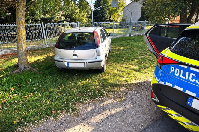 Srebrny Opel Corsa stoi na trawniku obok radiowozu. O zatrzymaniu pijanego kierowcy w Zawadach przeczytasz w Eska Siedlce.