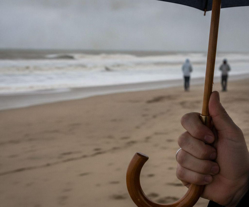 Dłoń osoby trzymającej parasol na tle pustej plaży i morza. O pogodzie we Władysławowie przeczytasz na Eska Trójmiasto.