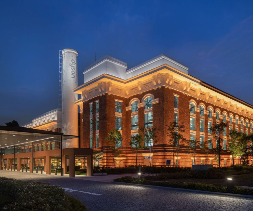 Zabytkowa elektrownia St James Power Station w Singapurze nocą, zaadaptowana na globalną siedzibę Dyson, z podświetloną ceglaną elewacją i białym kominem z logo firmy. Zdjęcie ilustruje, jak architektura industrialna może zyskać nowe życie, o czym więcej można przeczytać na Architektura Murator Plus.