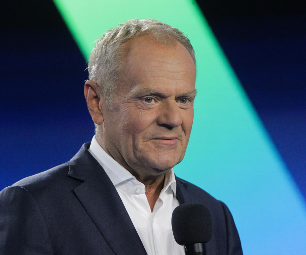 Premier Donald Tusk z mikrofonem na tle niebiesko-zielonego oświetlenia. O jego przesłaniu przeczytasz na SE Polityka.