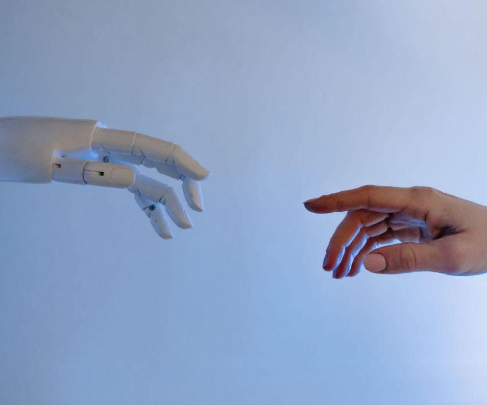 Dłoń robota i dłoń człowieka niemal się dotykają. O roli AI w pracy twórców przeczytasz na Eska.