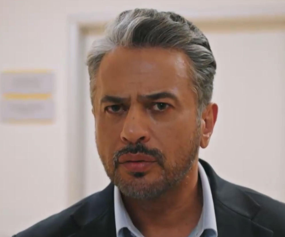 Mężczyzna o siwych włosach i brodzie, ubrany w marynarkę, patrzy z powagą, co odzwierciedla napięcie wokół testów DNA Orhana i podstępu Betul w serialu Złoty chłopak, o czym przeczytasz więcej na Super Seriale.