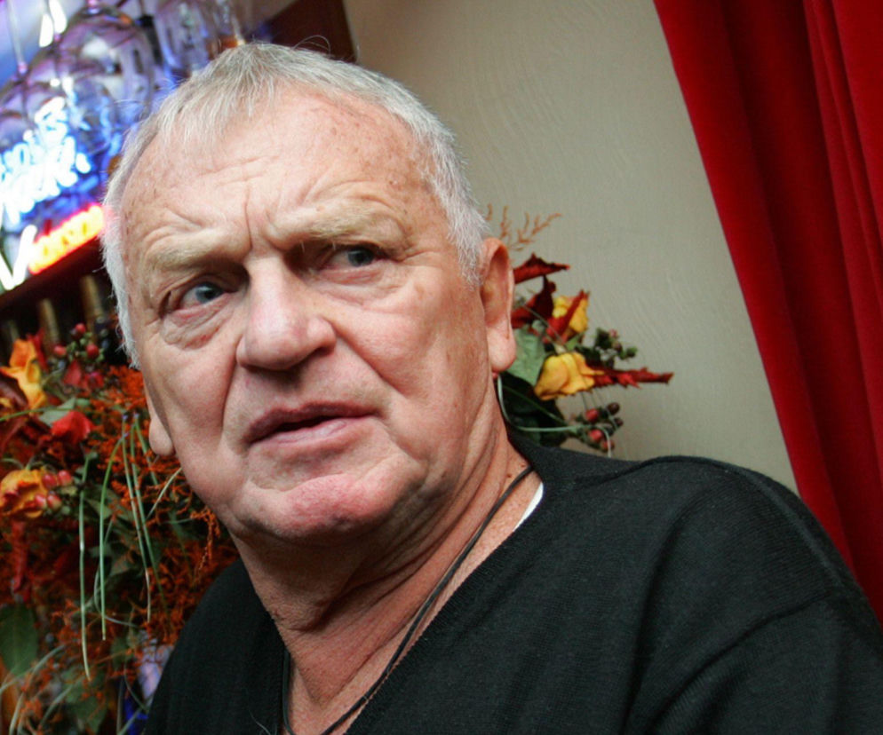 Portret Jerzego Gruzy w czarnym swetrze na tle czerwonej zasłony. O jego małżeństwie na odległość przeczytasz na SE.