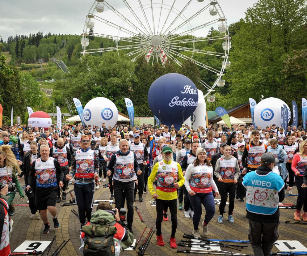 Tłum uczestników marszu nordic walking z kijkami, wielu w koszulkach z logo „Bieg po Nowe Życie”, w tle biały balon PZU i niebieski balon „Hotel Gołębiewski” oraz diabelski młyn, w Wiśle na 29. edycji promującej transplantologię w Polsce. Więcej o wydarzeniu na Poradnik Zdrowie.