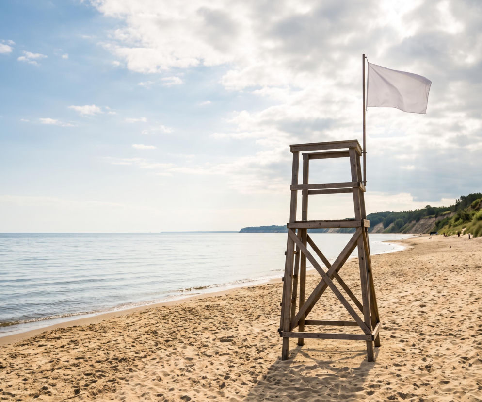 Wieża ratownicza z białą flagą na piaszczystej plaży w Trzęsaczu. O braku sinic przeczytasz na SE Szczecin.