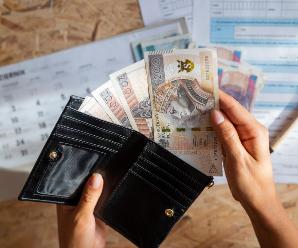 Dłonie osoby wyjmującej banknoty 200 złotych z czarnego portfela. O walce o zwrot pieniędzy z banku przeczytasz na SE.