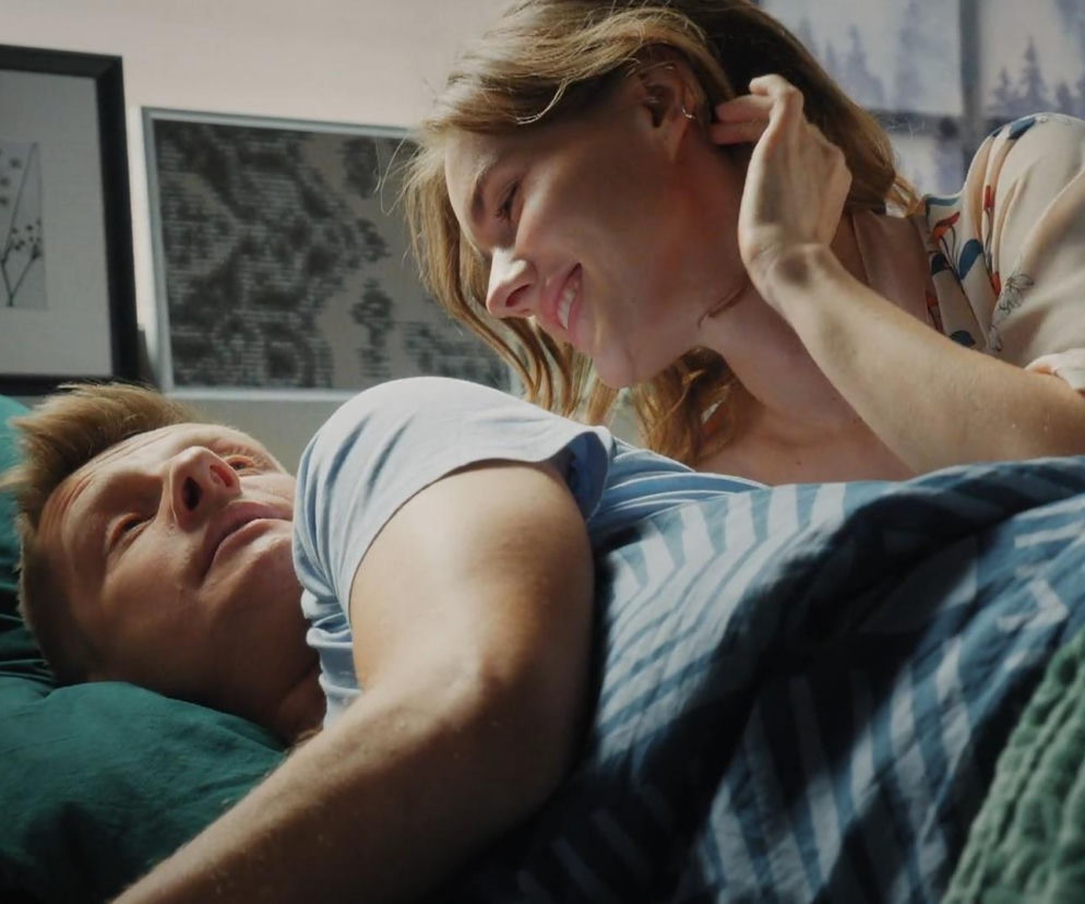 Uśmiechnięta Franka (Dominika Kachlik) pochyla się nad śpiącym Pawłem (Rafał Mroczek), delikatnie gładząc jego włosy, co jest częścią jego snu w 1908 odcinku M jak miłość. Para leży w łóżku, a Franka ma na sobie wzorzystą koszulę. Więcej o tym na Super Seriale.