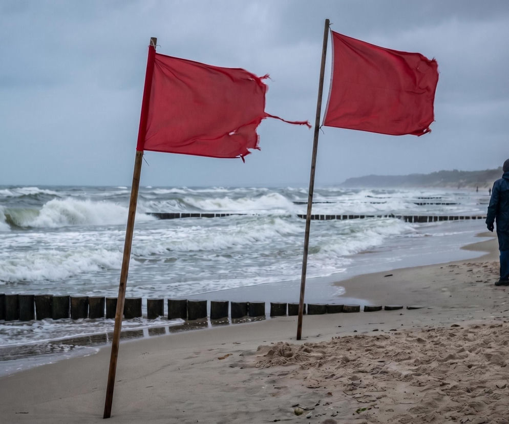 Dwie czerwone flagi na brzegu spienionego Bałtyku. Ludzie spacerują po plaży. O zakazie kąpieli przeczytasz na Eska.