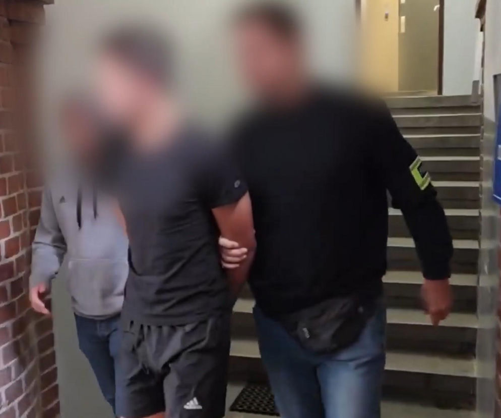 Policjant prowadzi skutego mężczyznę przez korytarz. O zatrzymaniu sprawców napadu we Wrocławiu przeczytasz na SE Wrocław.