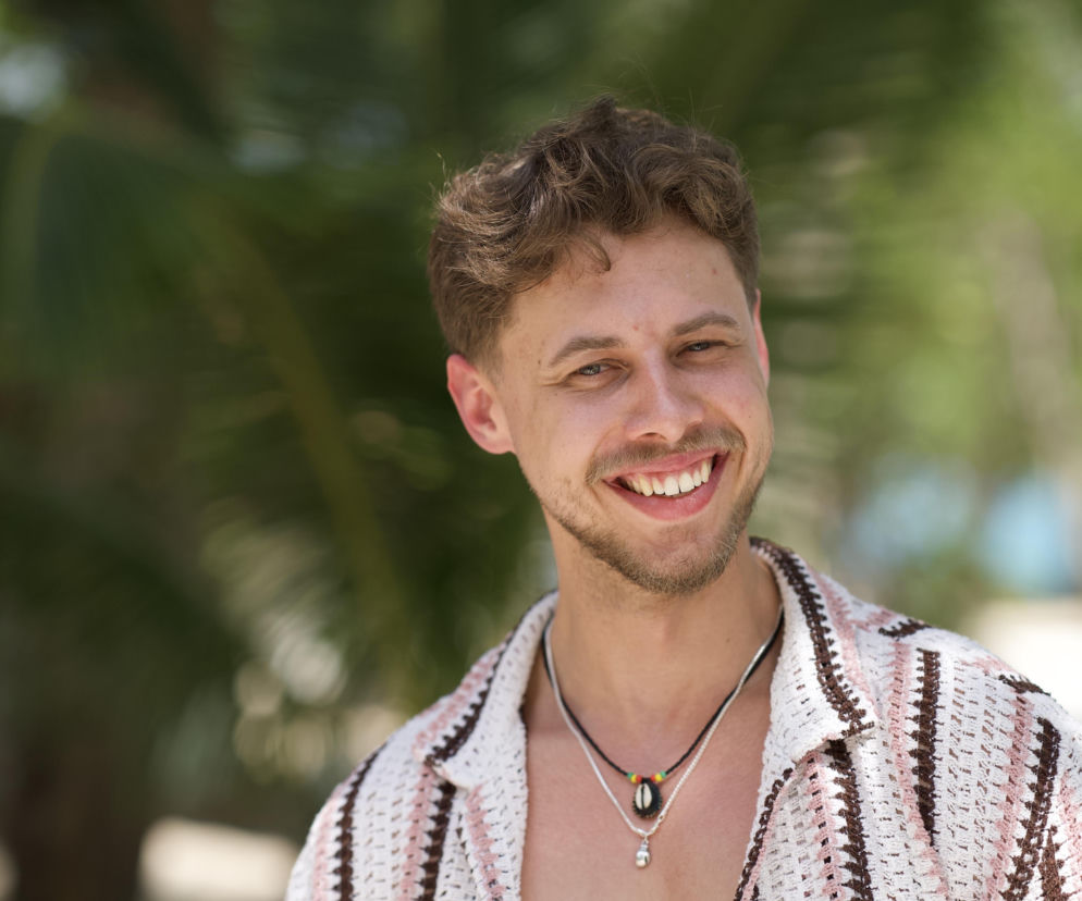 Uśmiechnięty Wiktor Borzych z Hotelu Paradise 13 na tle roślinności. O nowym uczestniku przeczytasz na VOX FM.