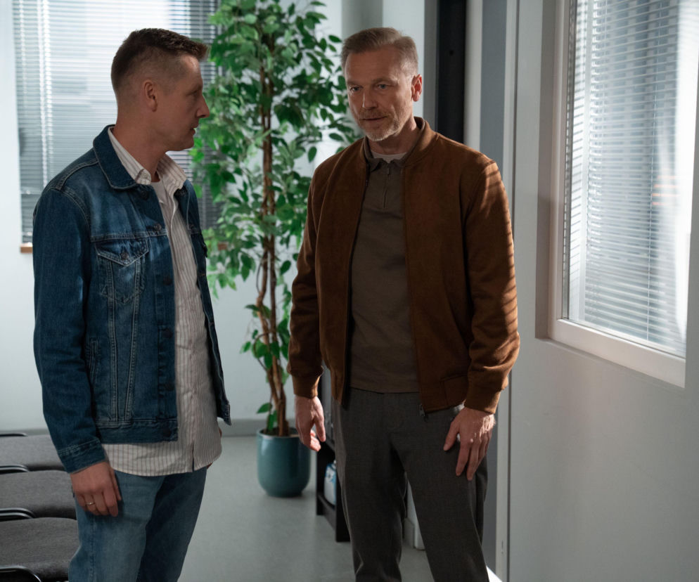 Rafał Mroczek jako Paweł Zduński w dżinsowej kurtce i Krystian Wieczorek jako Andrzej Budzyński w brązowej kurtce, rozmawiający w jasnym pomieszczeniu. Scena pokazuje ich obawy po pogrzebie Franki, co szczegółowo omawiamy na Super Seriale.